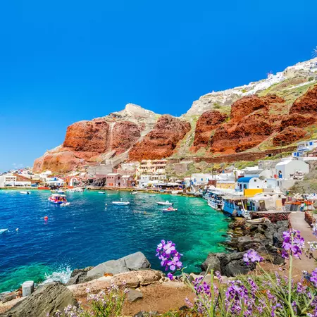 A bay framed by red cliffs dotted with small whitewashed buildings.
