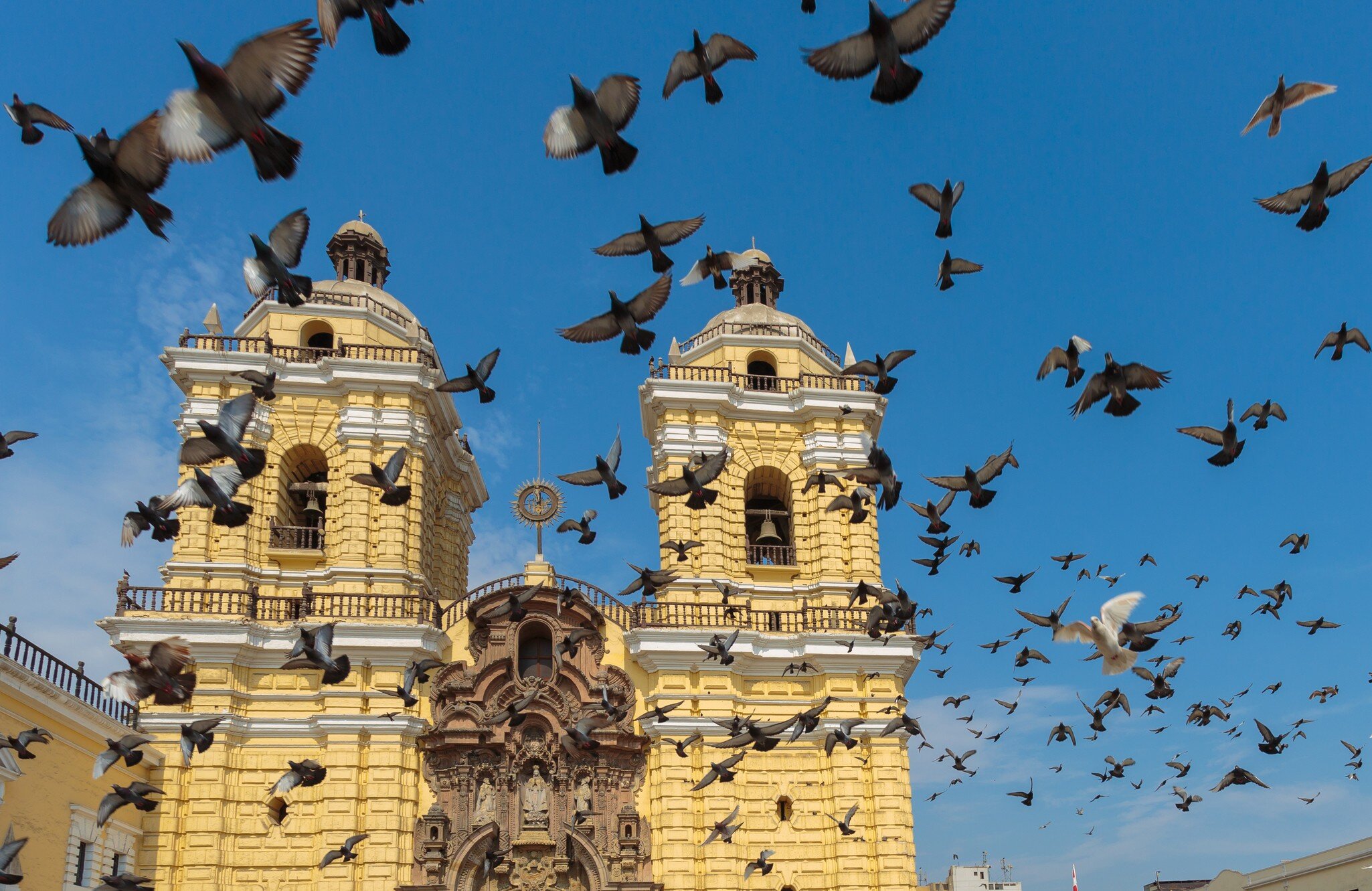 Birds fly around a yellow pillar on a religious building in Lima, Peru.