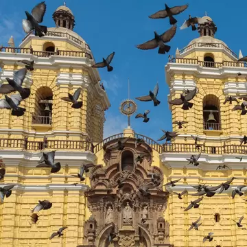 Birds fly around a yellow pillar on a religious building in Lima, Peru.