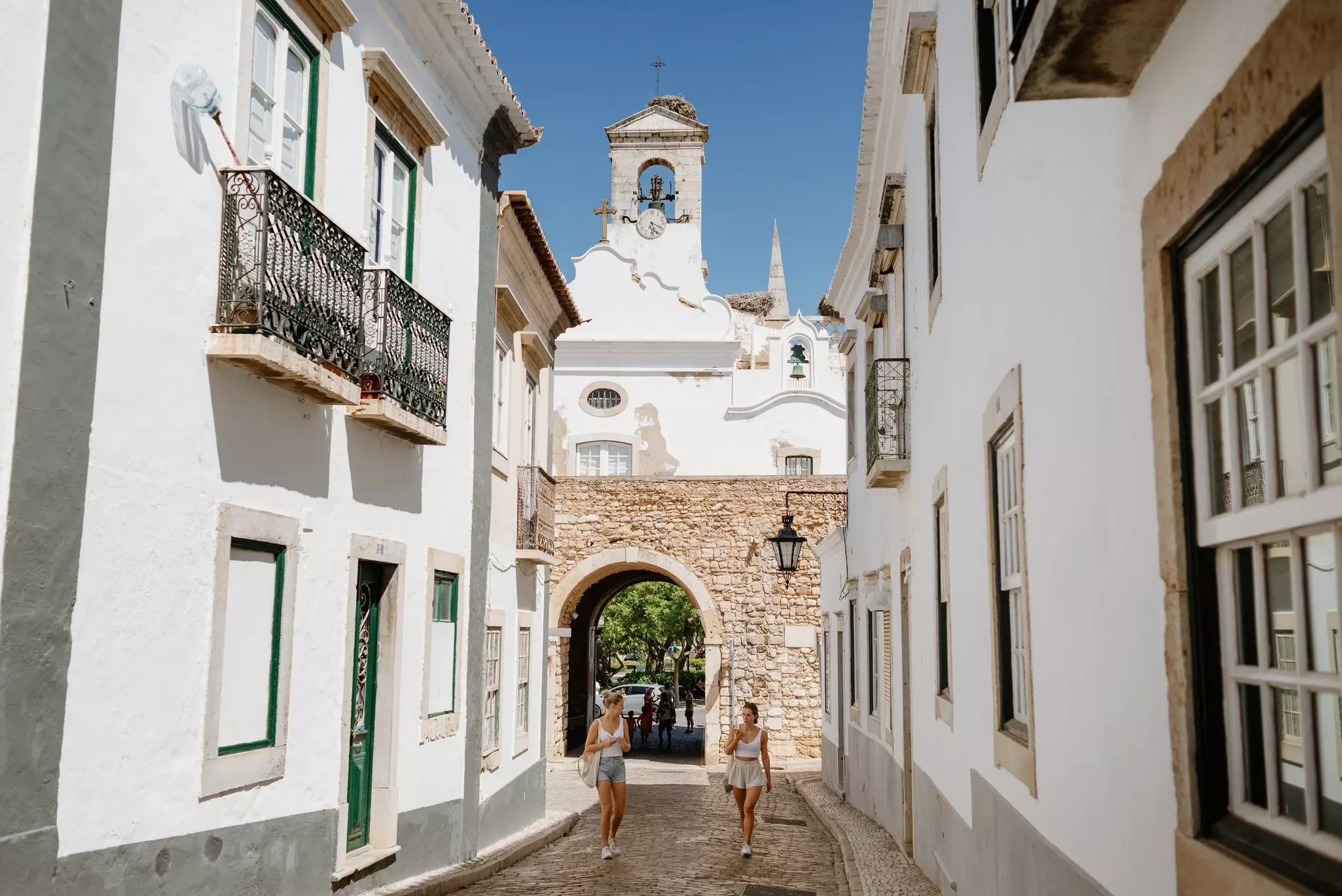 Two young tourist girls walk on a summer morning along a street in Faro, a city in the Algarve.