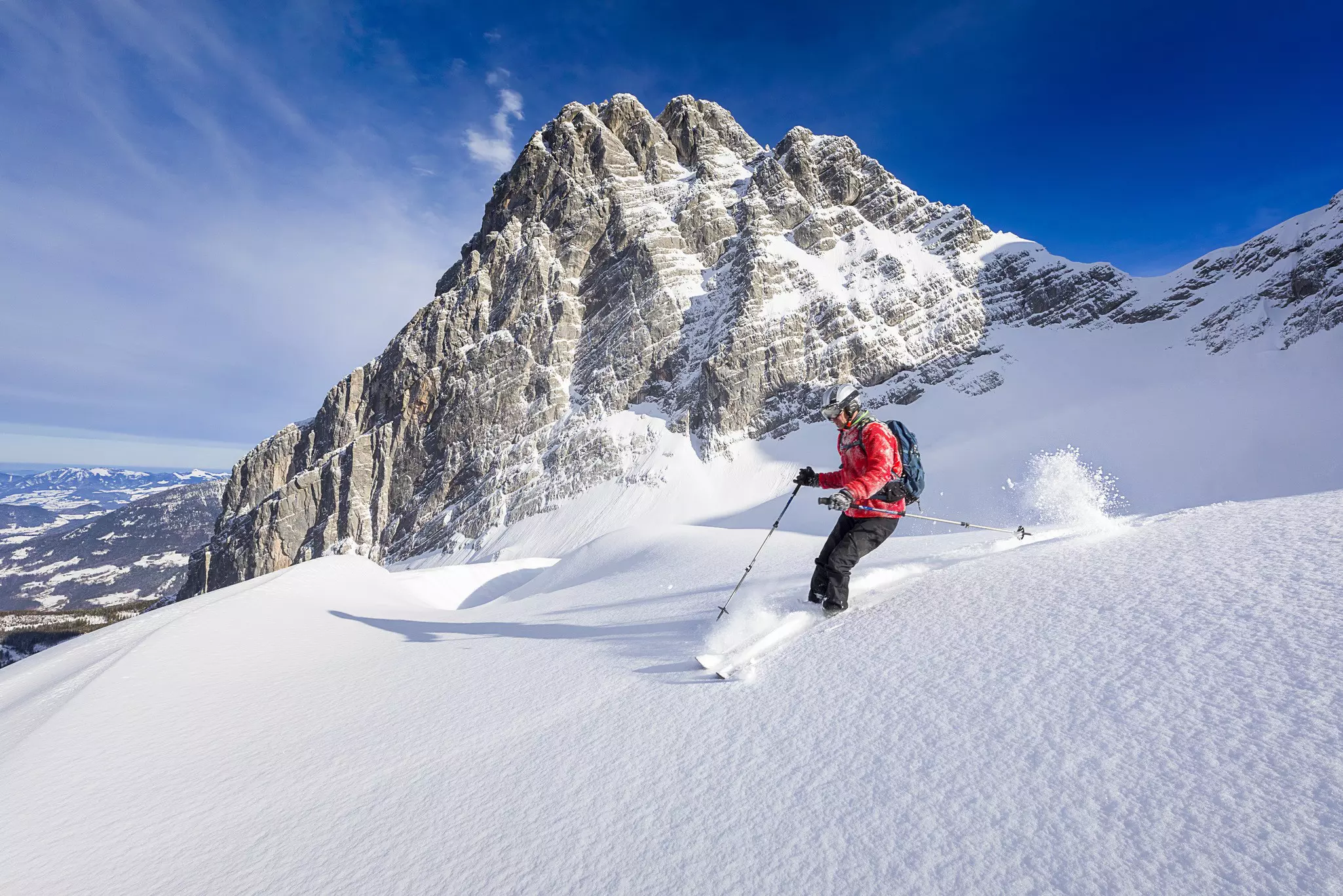 A man sking through powder in the back country of Berchtesgaden National Park; he's in a large track of virgin powder with a large pyramid rocky summit rising in the background.