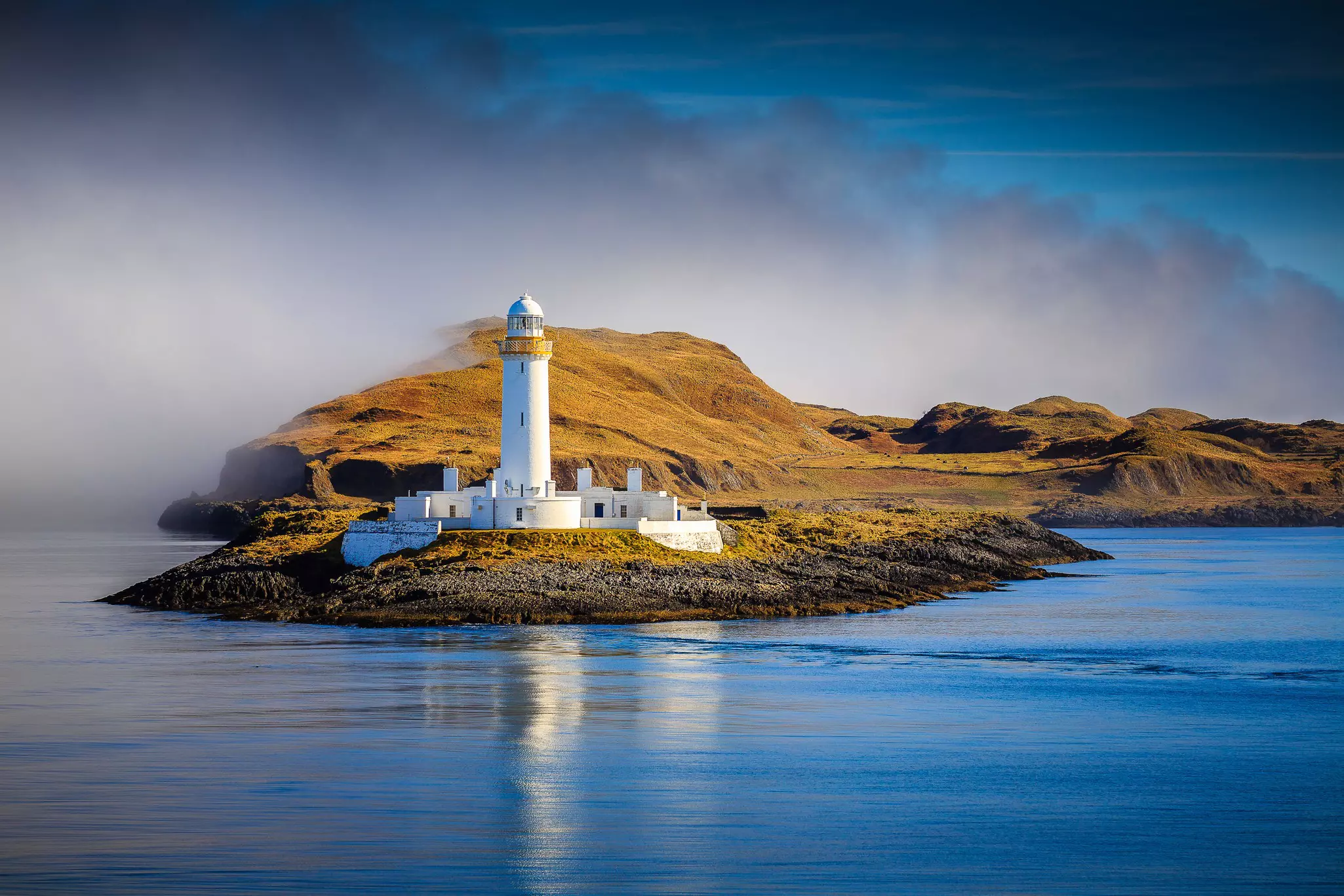 Sunny day view of the misty shoreline by the Lismore Lighthouse, Isle of Lismore, Scotland.