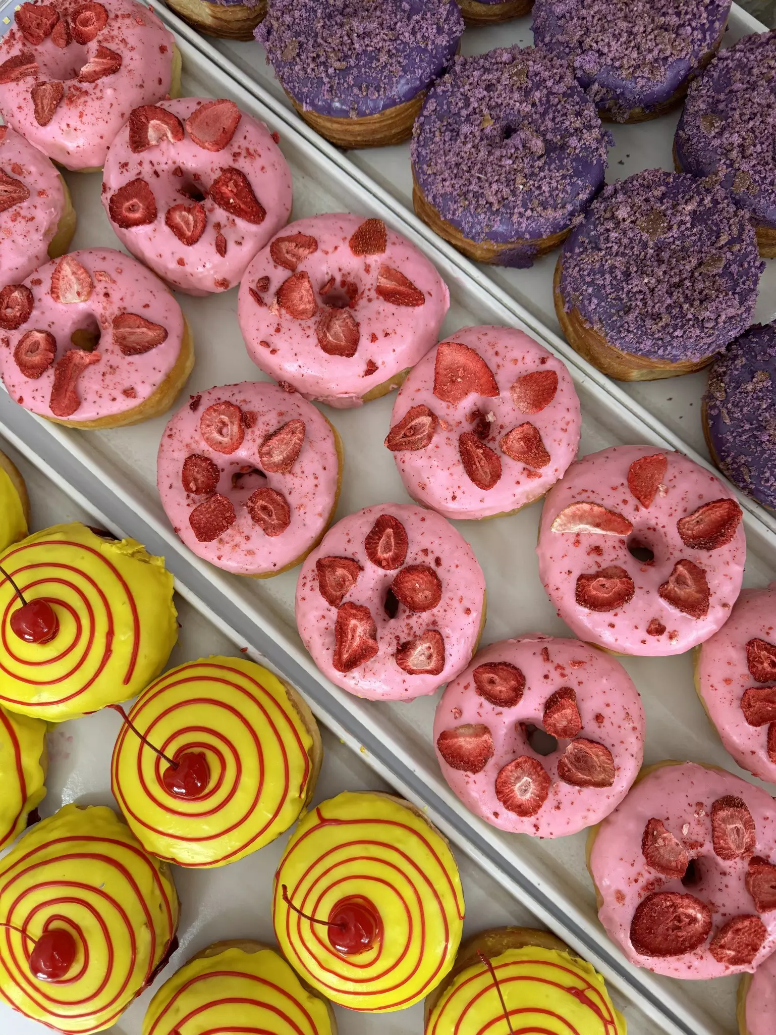 Rows of brightly colored yellow, pink and purple donuts on baking sheets
