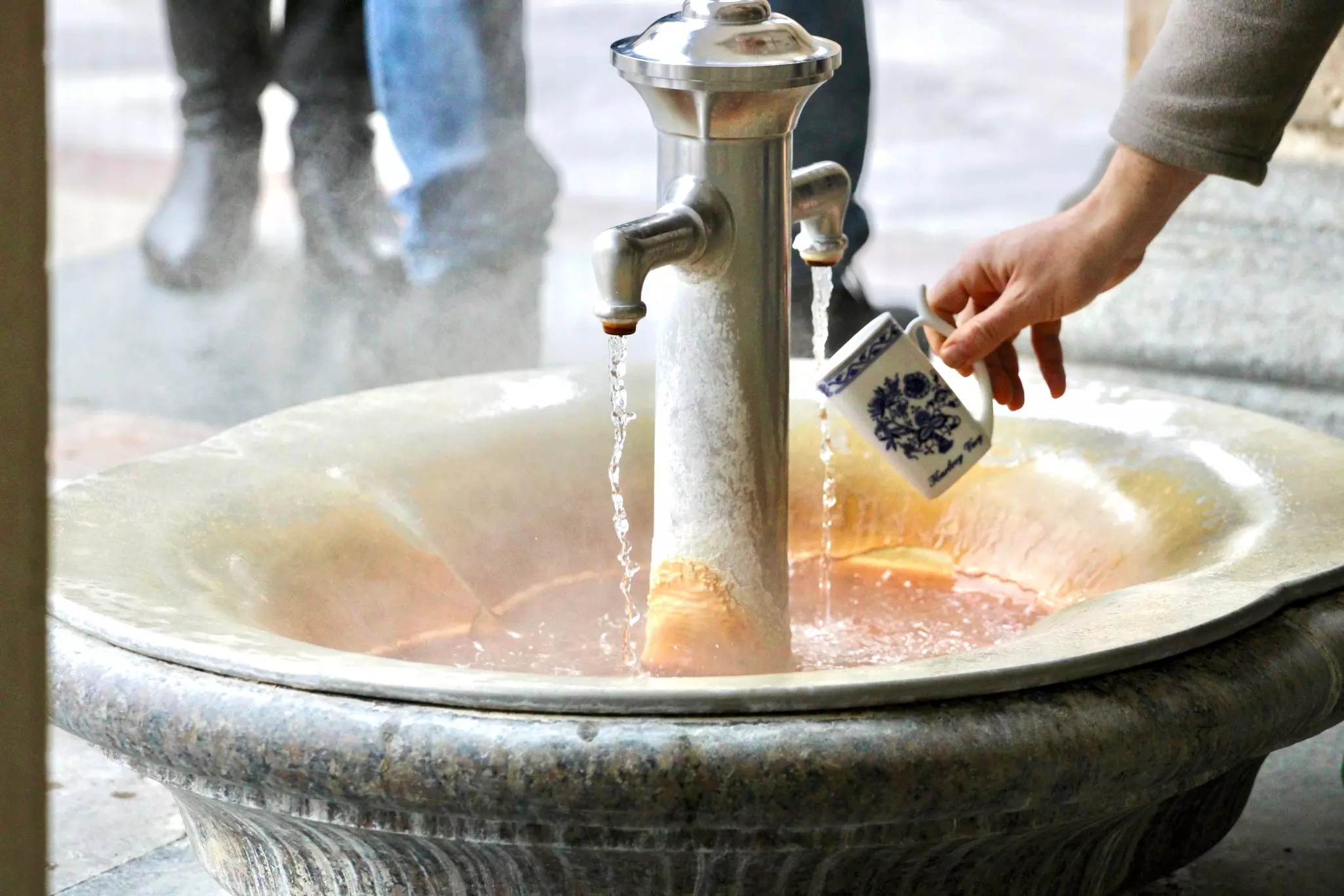 Hot mineral water source in the building The Mill Colonnade in Karlovy Vary, Czech Republic. Catching a water from hot mineral spring in Karlovy Vary, special mug.