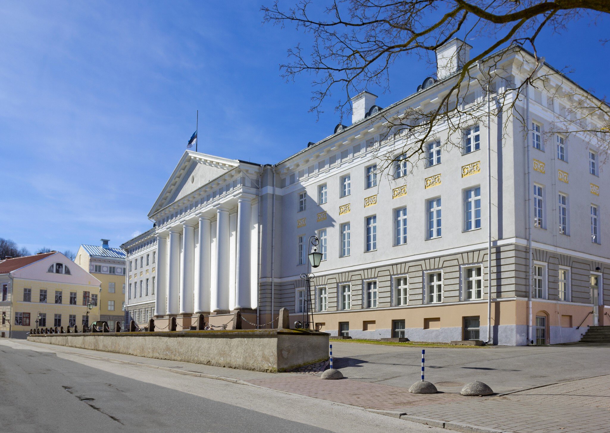 White neoclassical facade with a tall columned portico and gold window ornaments under a clear blue sky