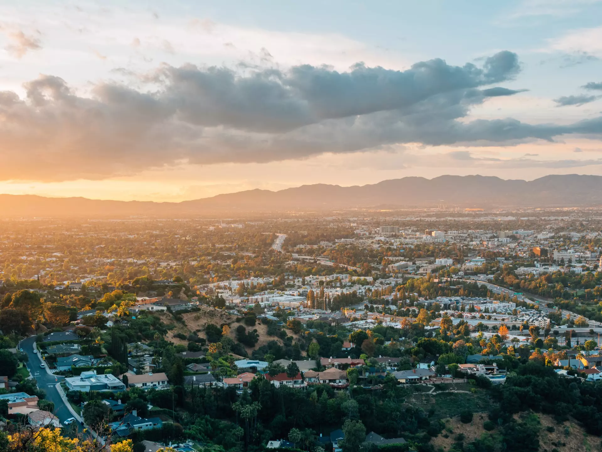 The sun setting over mountains with a green city in the foreground