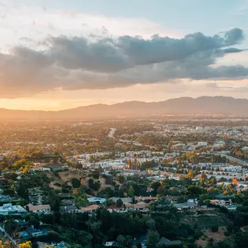 The sun setting over mountains with a green city in the foreground