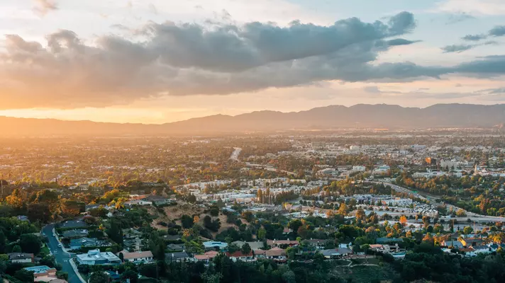 View of the sun setting over mountains with a green city in the foreground