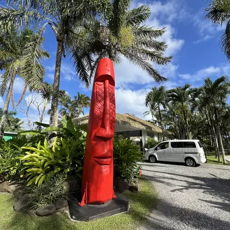 A large red sculture of an elongated head and face stands outside the entrance to a hotel surrounded by palm trees.