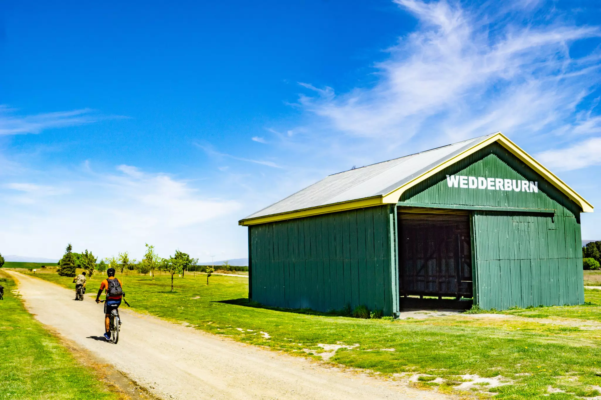 On the Central Otago Rail Trail, cyclists pass a landmark green rail shed at Wedderburn, New Zealand.
