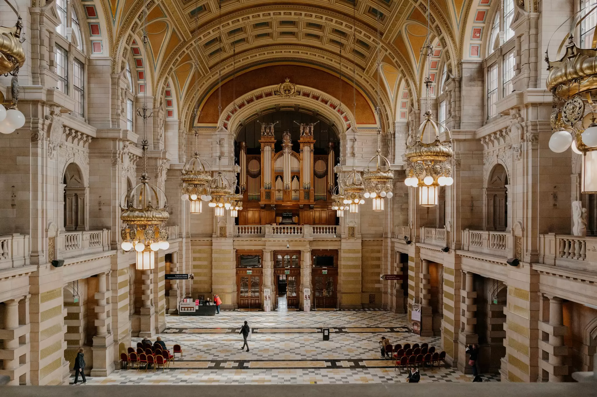 A large ornate hall, with a patterned tile floor and painted vaulted ceiling.