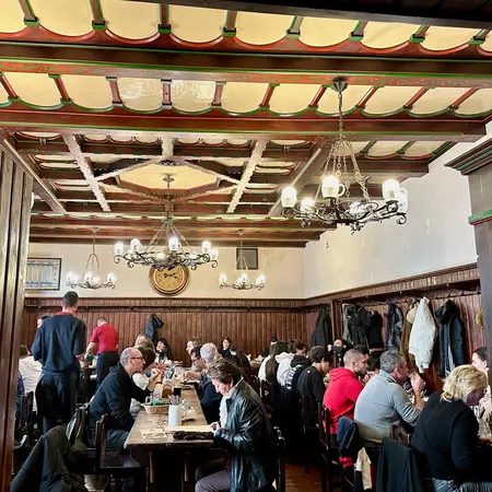 People sitting at tables in a room with partially wood-paneled walls. Chandeliers hang from the ceiling. 