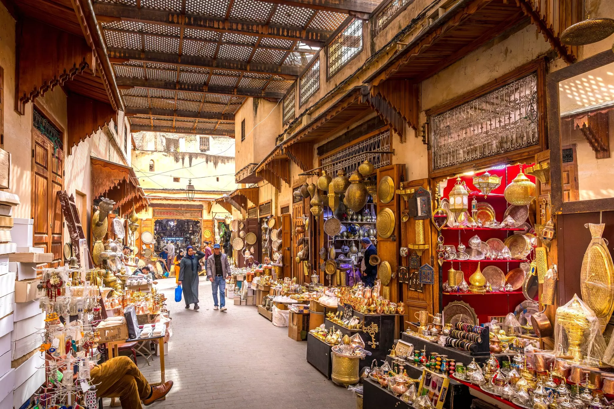Two shoppers stroll down a narrow street lined with stalls selling gifts and souvenirs of local crafts.