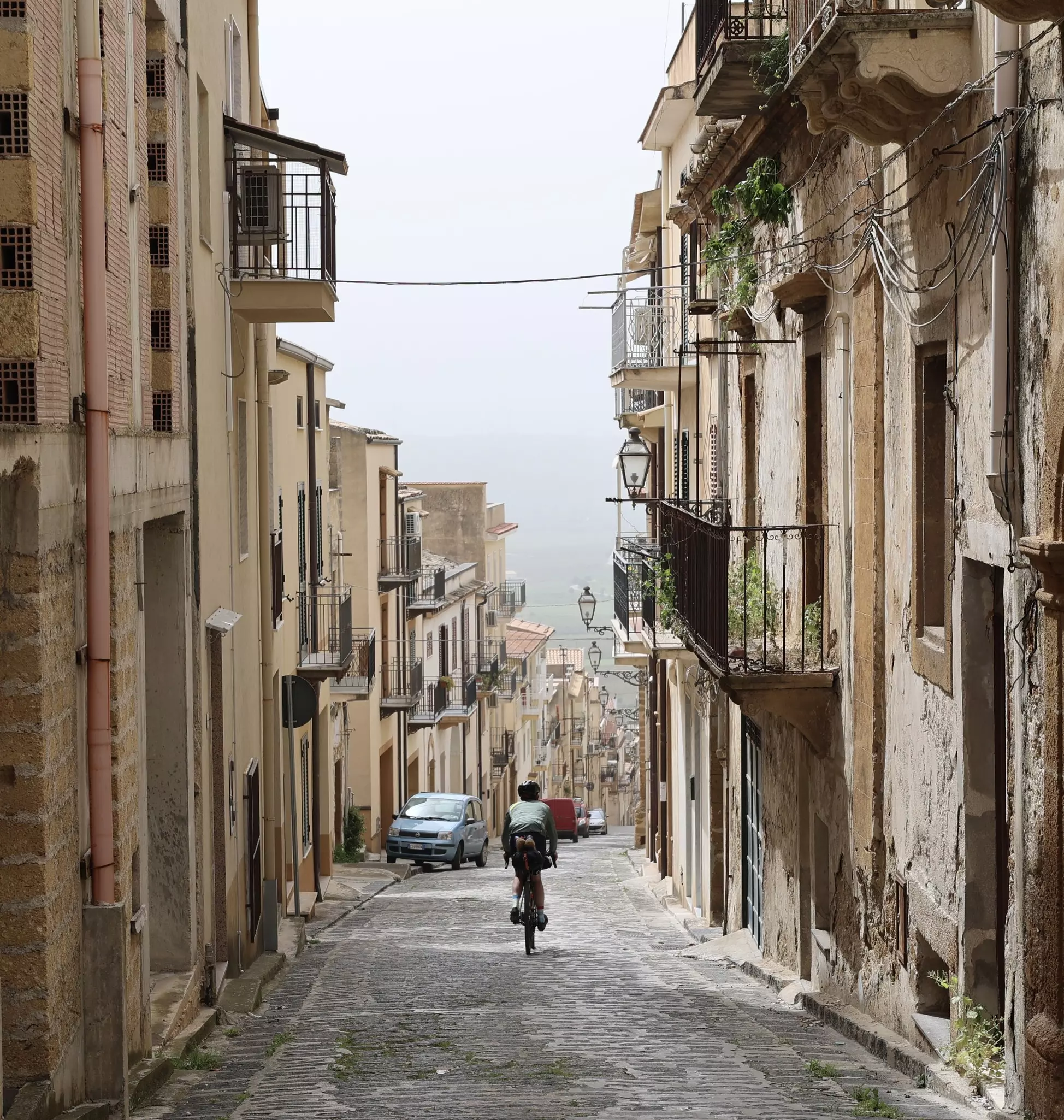 A cyclist wheels their way down a cobbled street in a hilltop village.