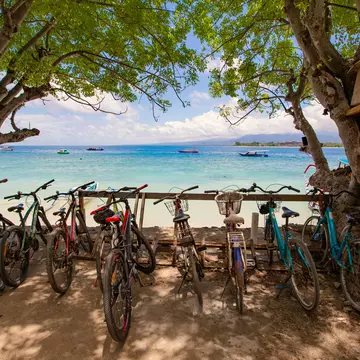 Bikes parked in a line along the edge of a beautiful sandy beach with blue water in Gili Island, Bali, Indonesia.