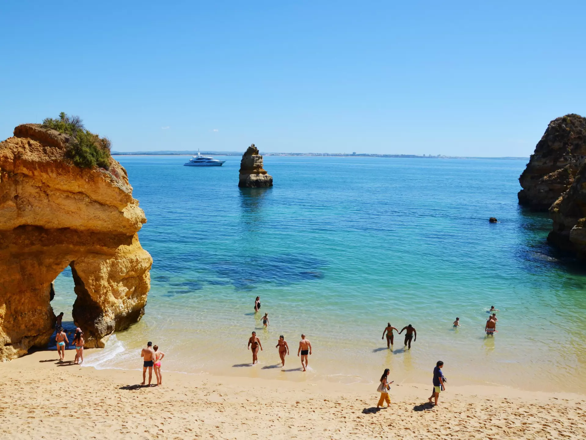 People in the shallows of the scenic Camilo Beach (Praia do Camilo) at Algarve, Portugal with turquoise sea in background