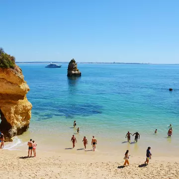People in the shallows of the scenic Camilo Beach (Praia do Camilo) at Algarve, Portugal with turquoise sea in background