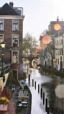 A split-level canal. On ground level, bicycles are parked at a railing; at the water level, empty outdoor tables sit beside the water.