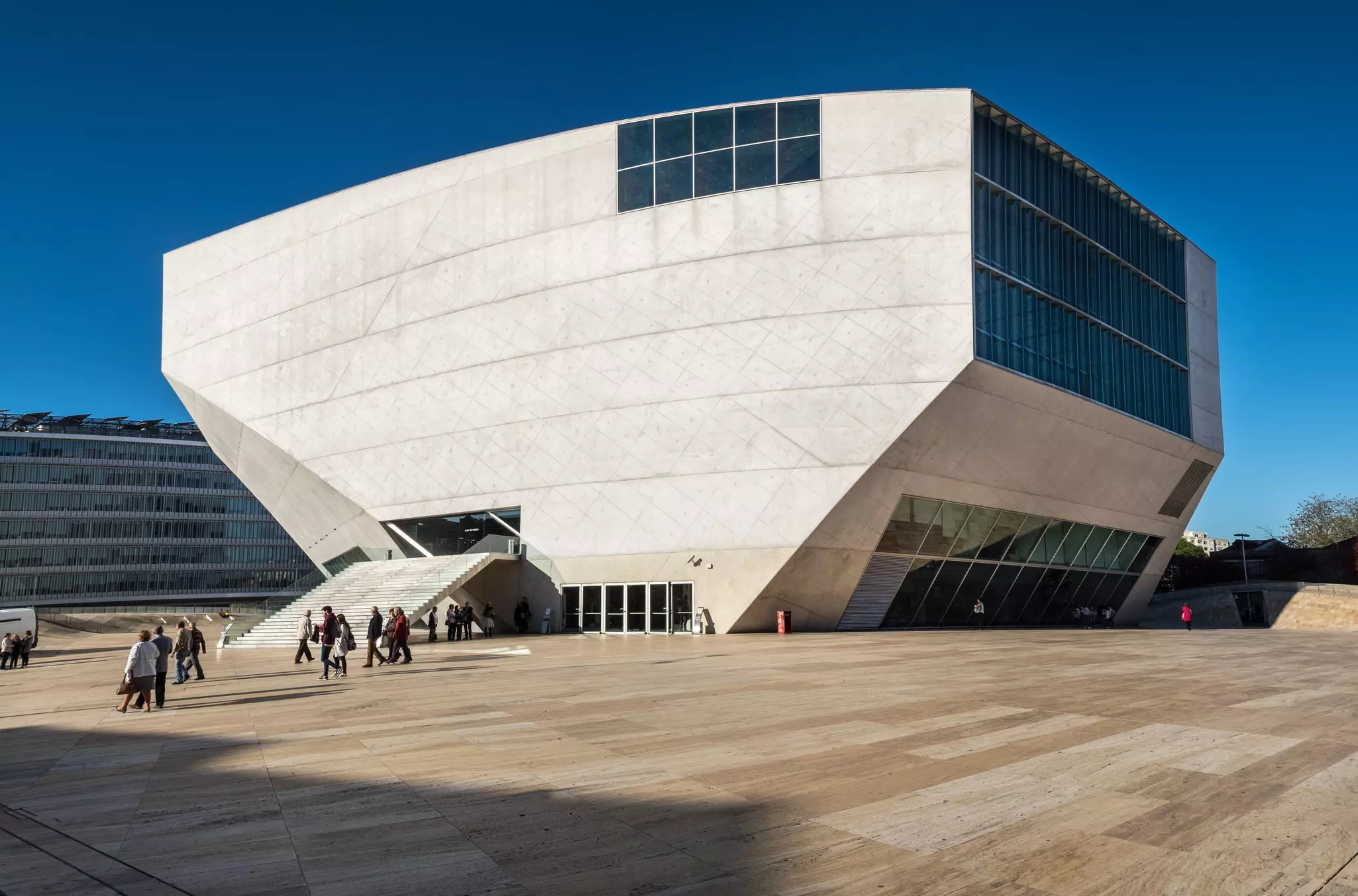 An angular modern building with an elevated stairway to the entrance is at the center of a large open plaza in Porto, Portugal.