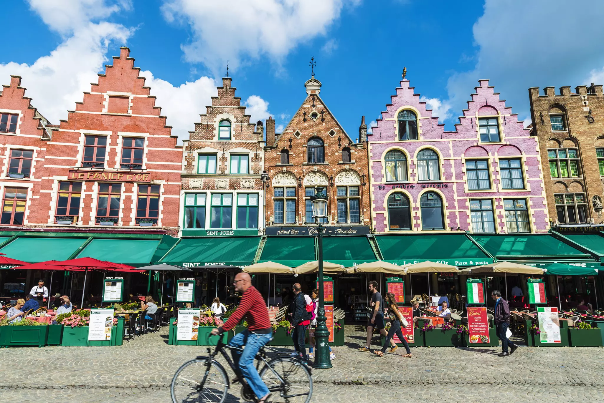 A man on a bicycle pedals pas restaurants in historic buildings on a large square.
