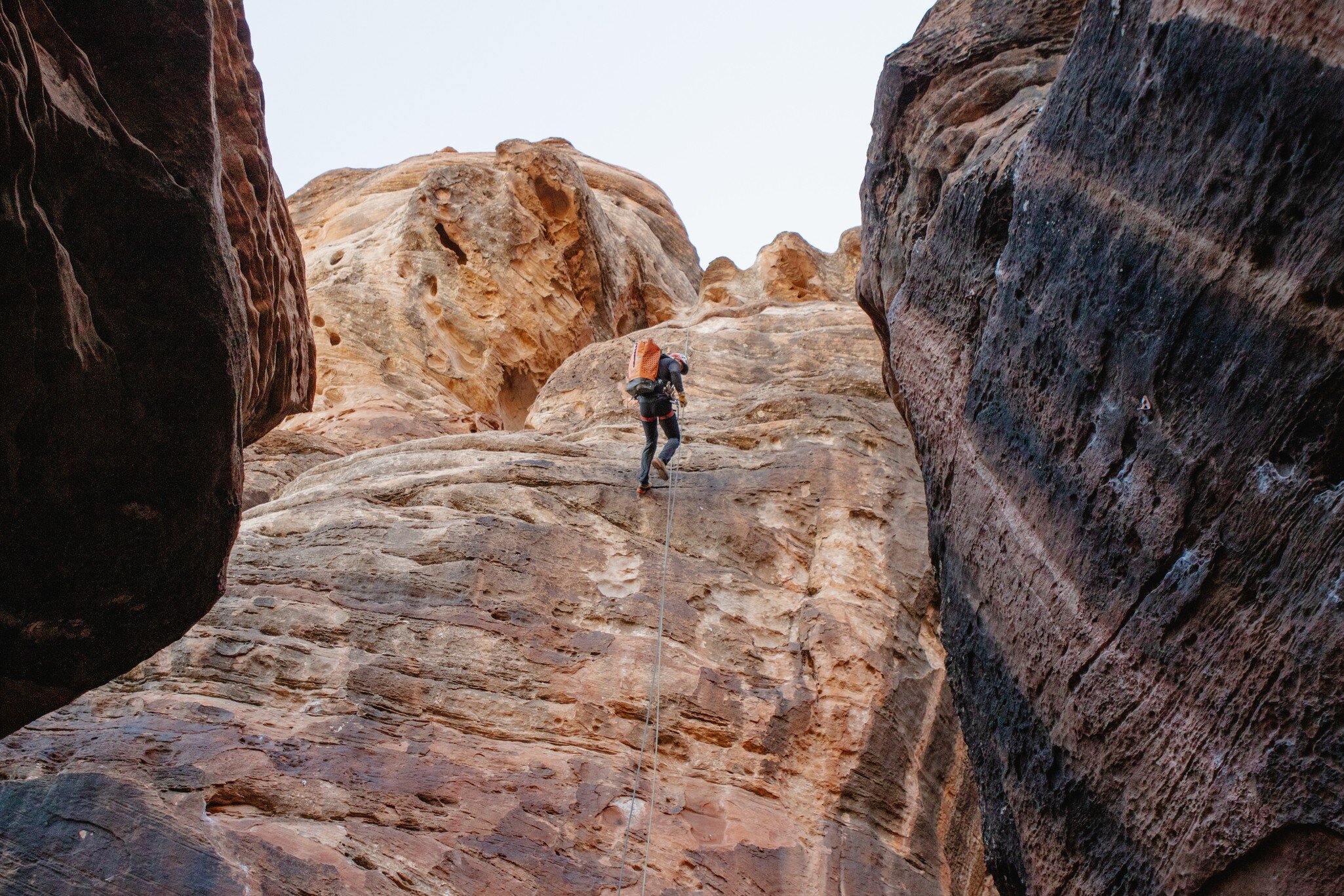 Canyoneer with an orange pack rappels down a sandstone wall between dark rock in Zion National Park, Utah