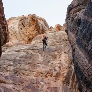 Canyoneer with an orange pack rappels down a sandstone wall between dark rock in Zion National Park, Utah