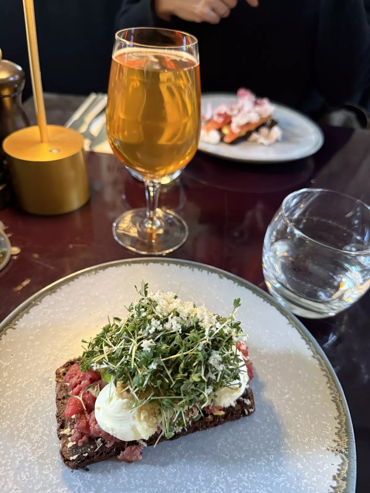 Close-up of beef tartare smørrebrød on a plate with glasses in the background.