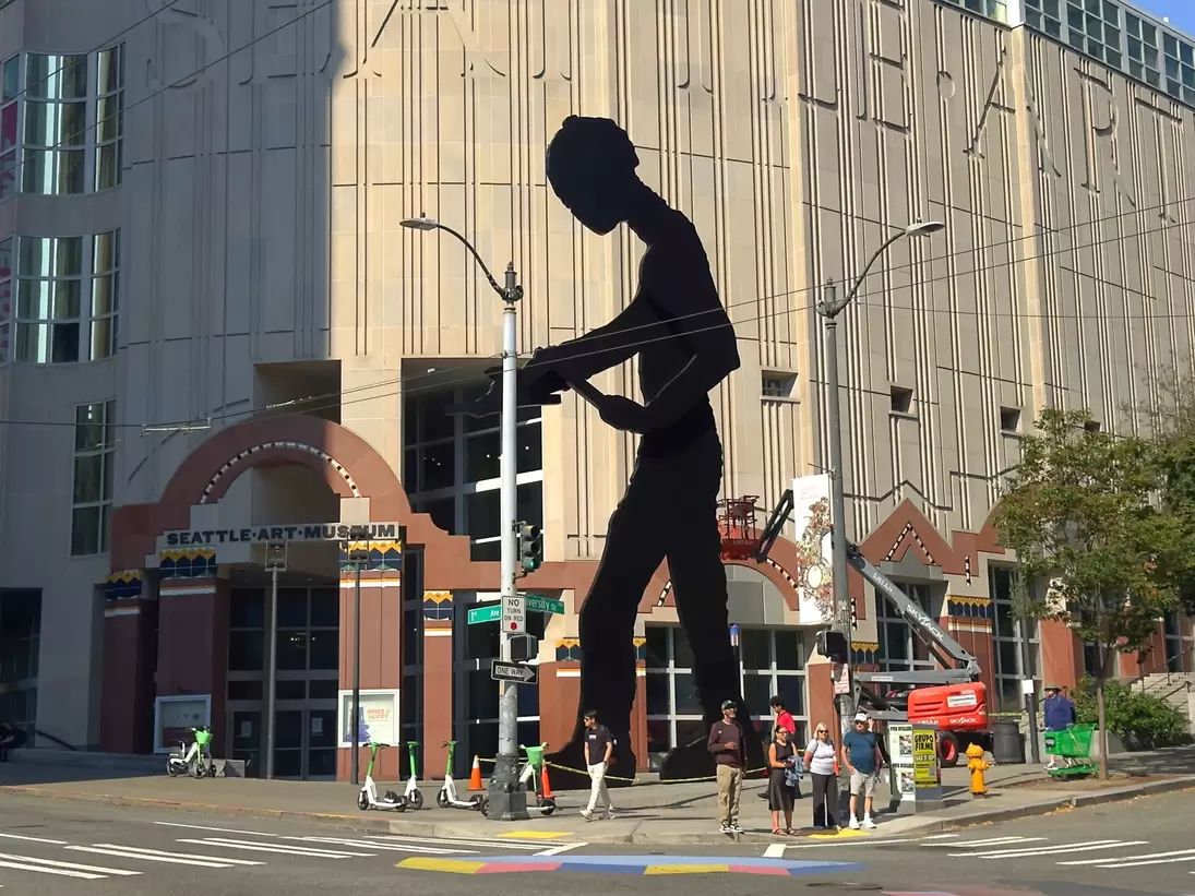 Giant black steel figure with raised hammer at 1st Ave and University St, Seattle Art Museum entrance and pedestrians below