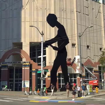 Giant black steel figure with raised hammer at 1st Ave and University St, Seattle Art Museum entrance and pedestrians below