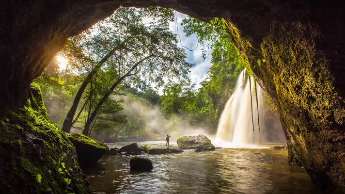 A person stands staring at a beautiful waterfall through a large stone arch