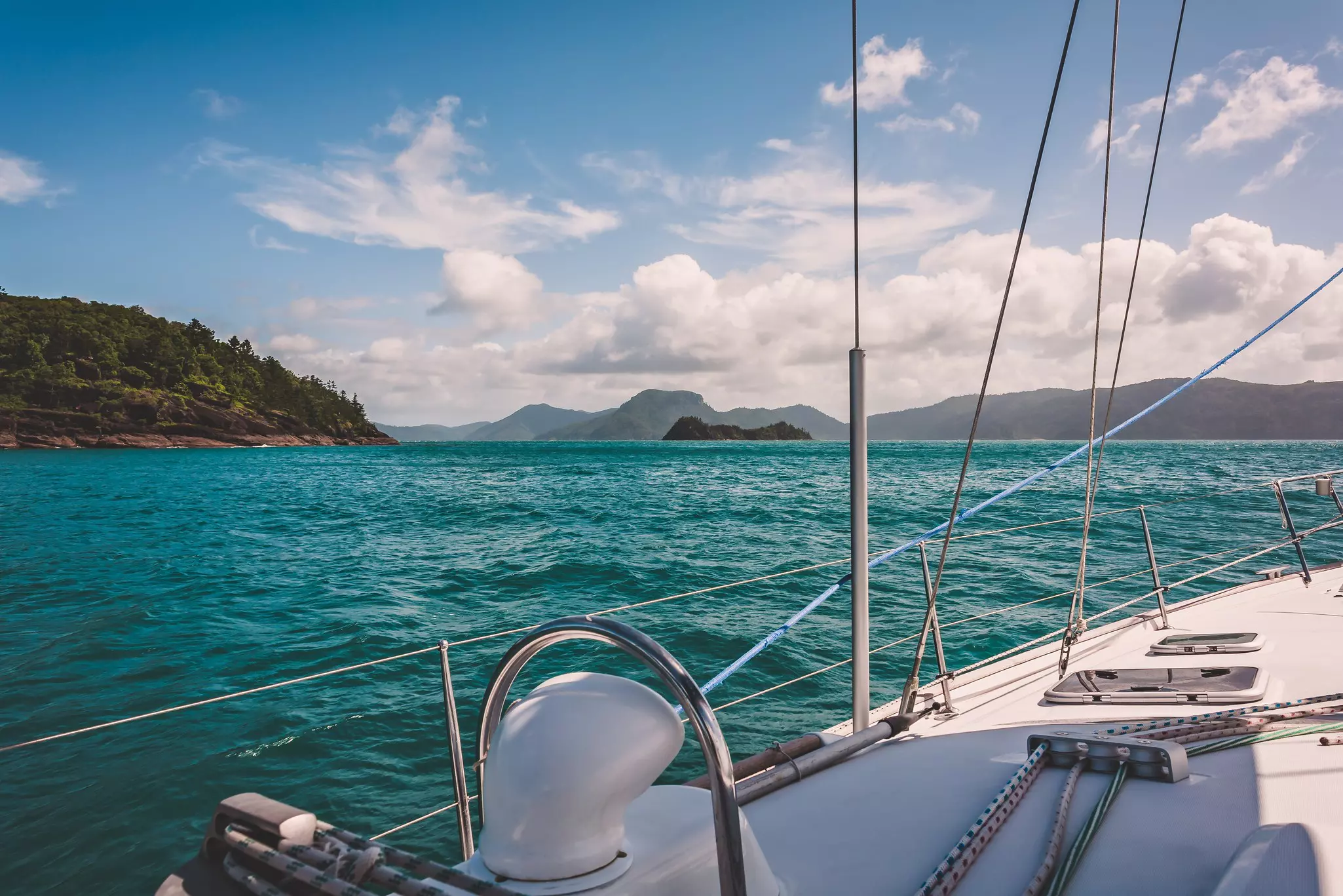 Blue-green water makes gentle waves around the side of a white sailboat in Australia's Whitsunday Islands.