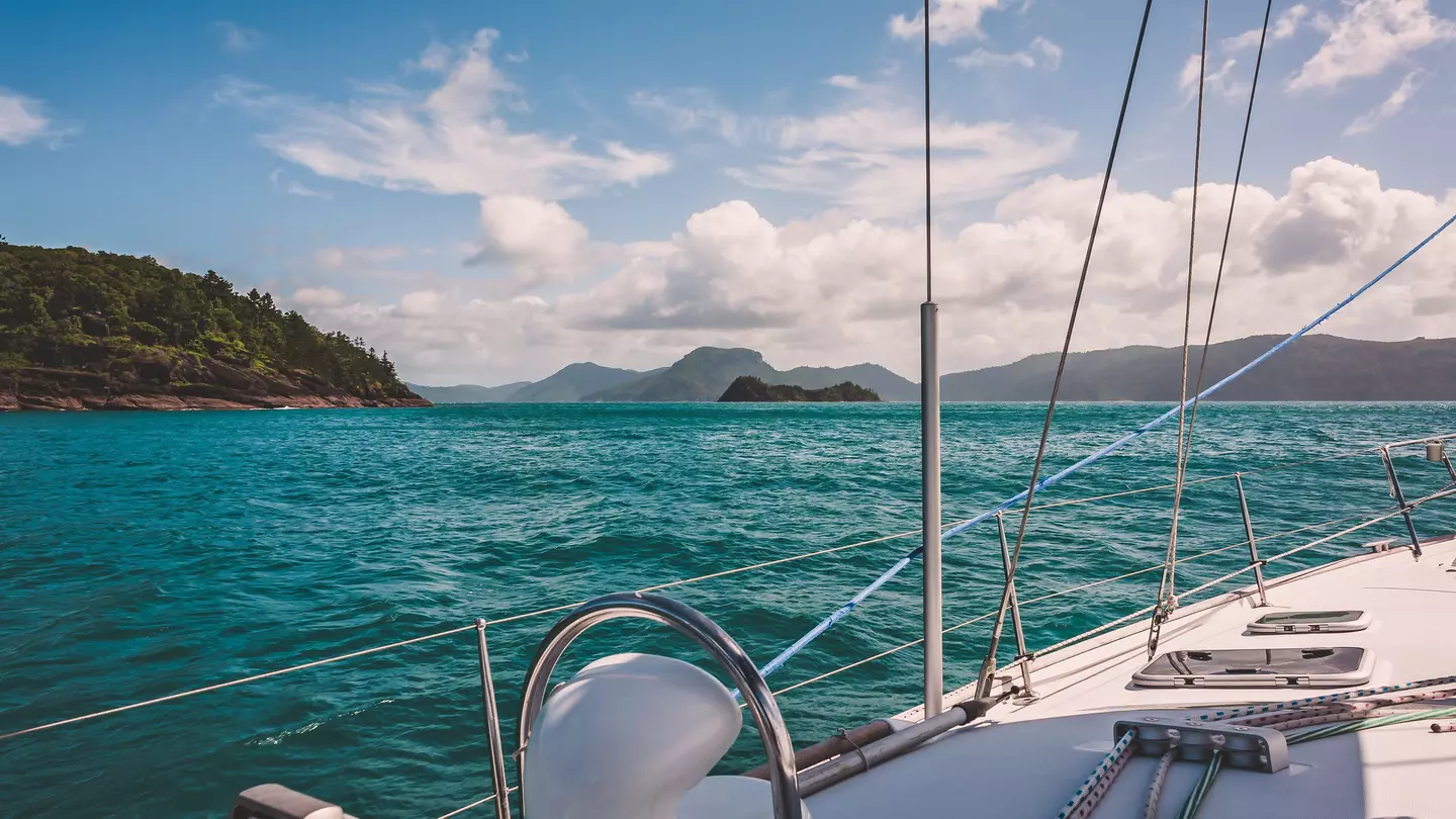 Blue-green water makes gentle waves around the side of a white sailboat in Australia's Whitsunday Islands.