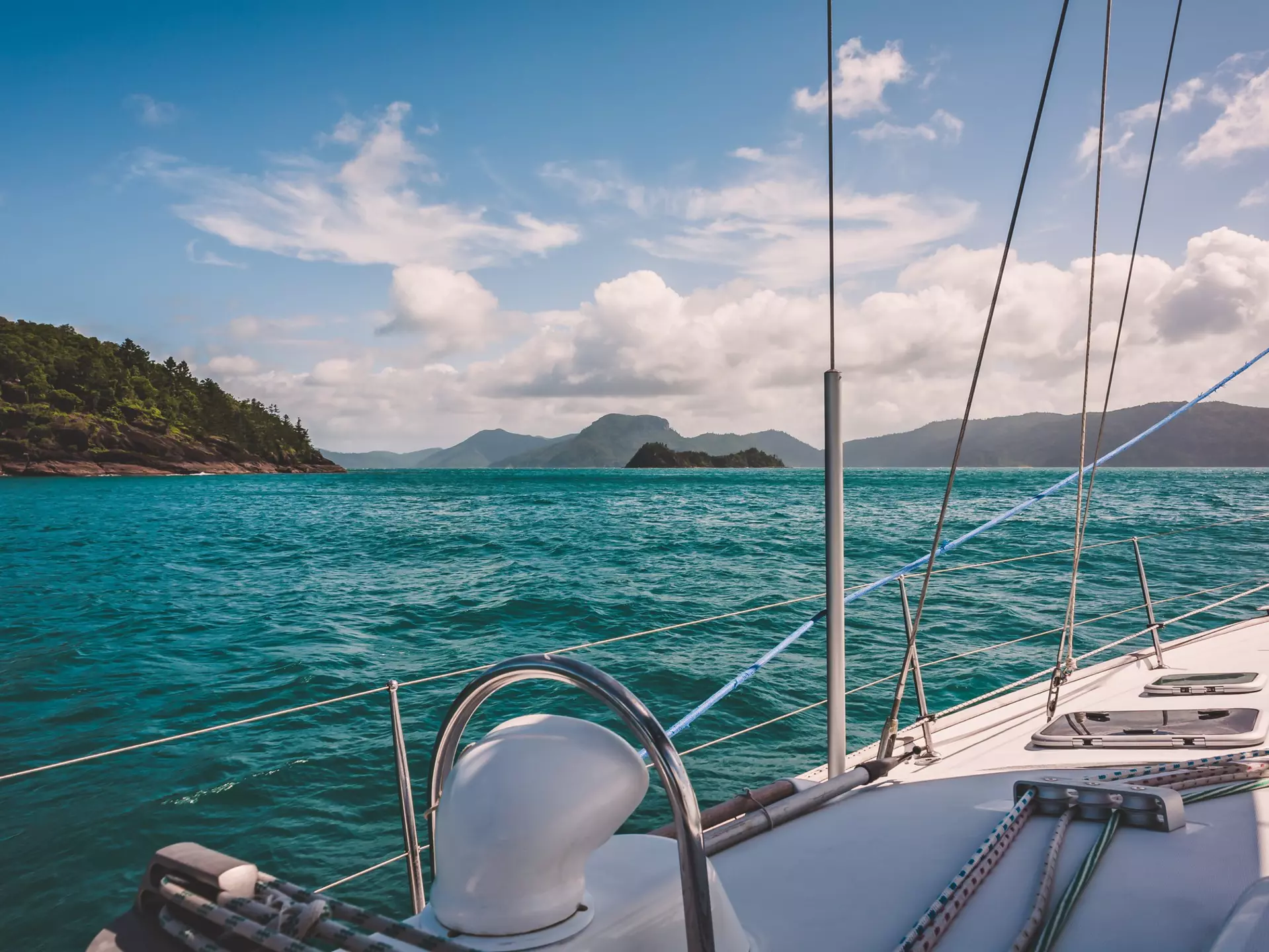 Blue-green water makes gentle waves around the side of a white sailboat in Australia's Whitsunday Islands.
