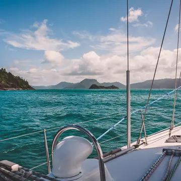 Blue-green water makes gentle waves around the side of a white sailboat in Australia's Whitsunday Islands.