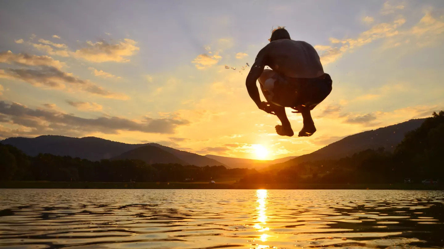 Young man jump onto summer water during calm sunset