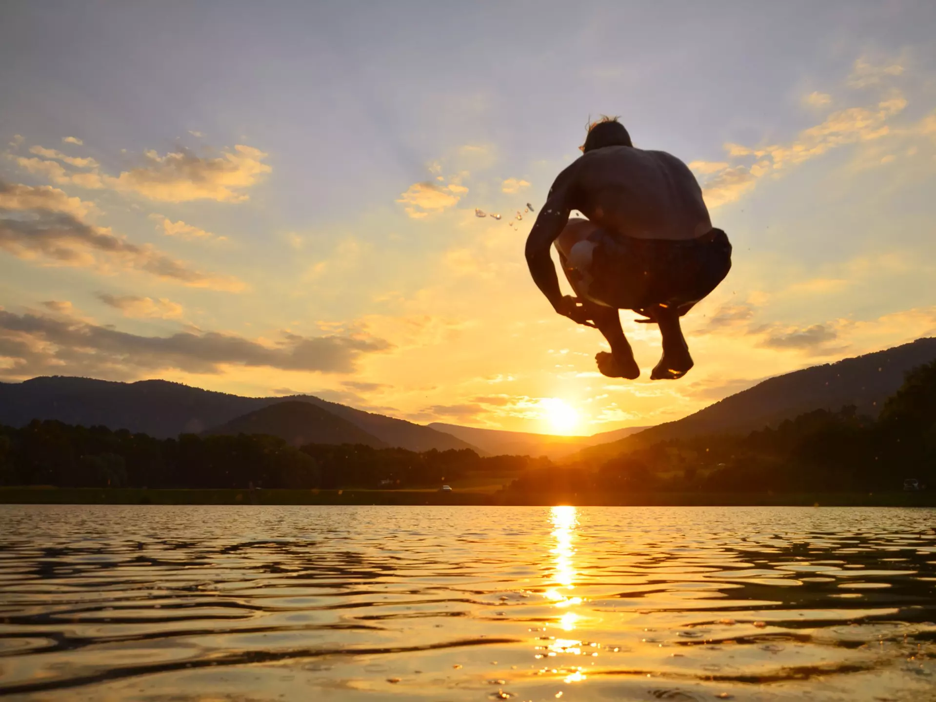 Young man jump onto summer water during calm sunset