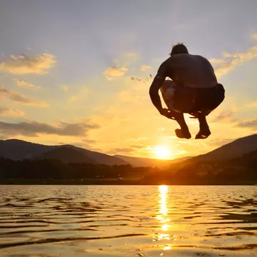 Young man jump onto summer water during calm sunset