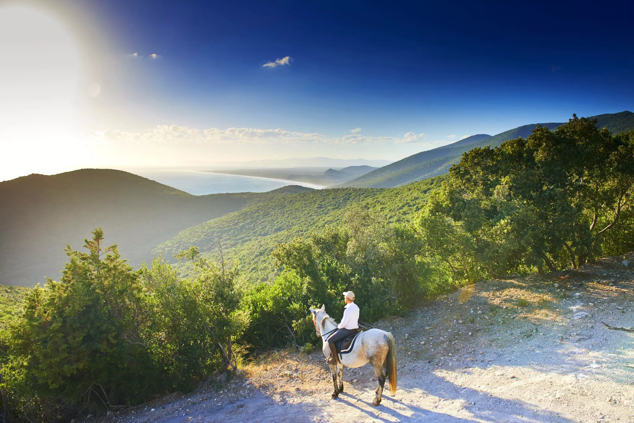 A man on horseback looks out at a dramatically lit valley in a beautiful nature park.