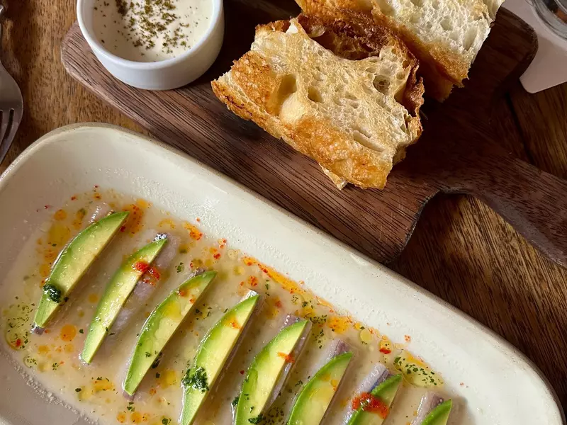 Slices of avocado on top of slices of white fish resting in a thin sauce on a white dish.