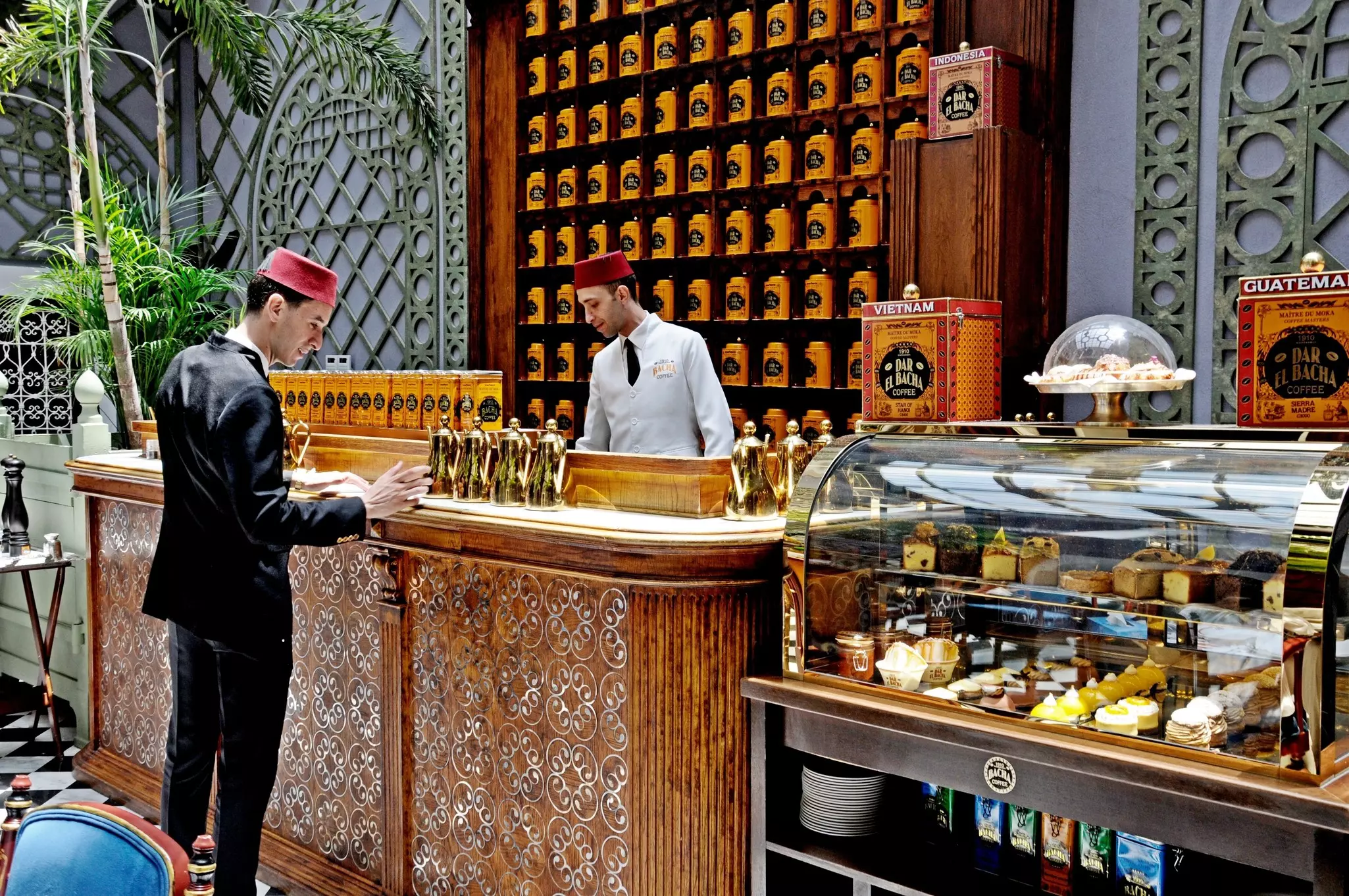 Two servers in a coffee shop with a wall of coffee beans and tiled decor.