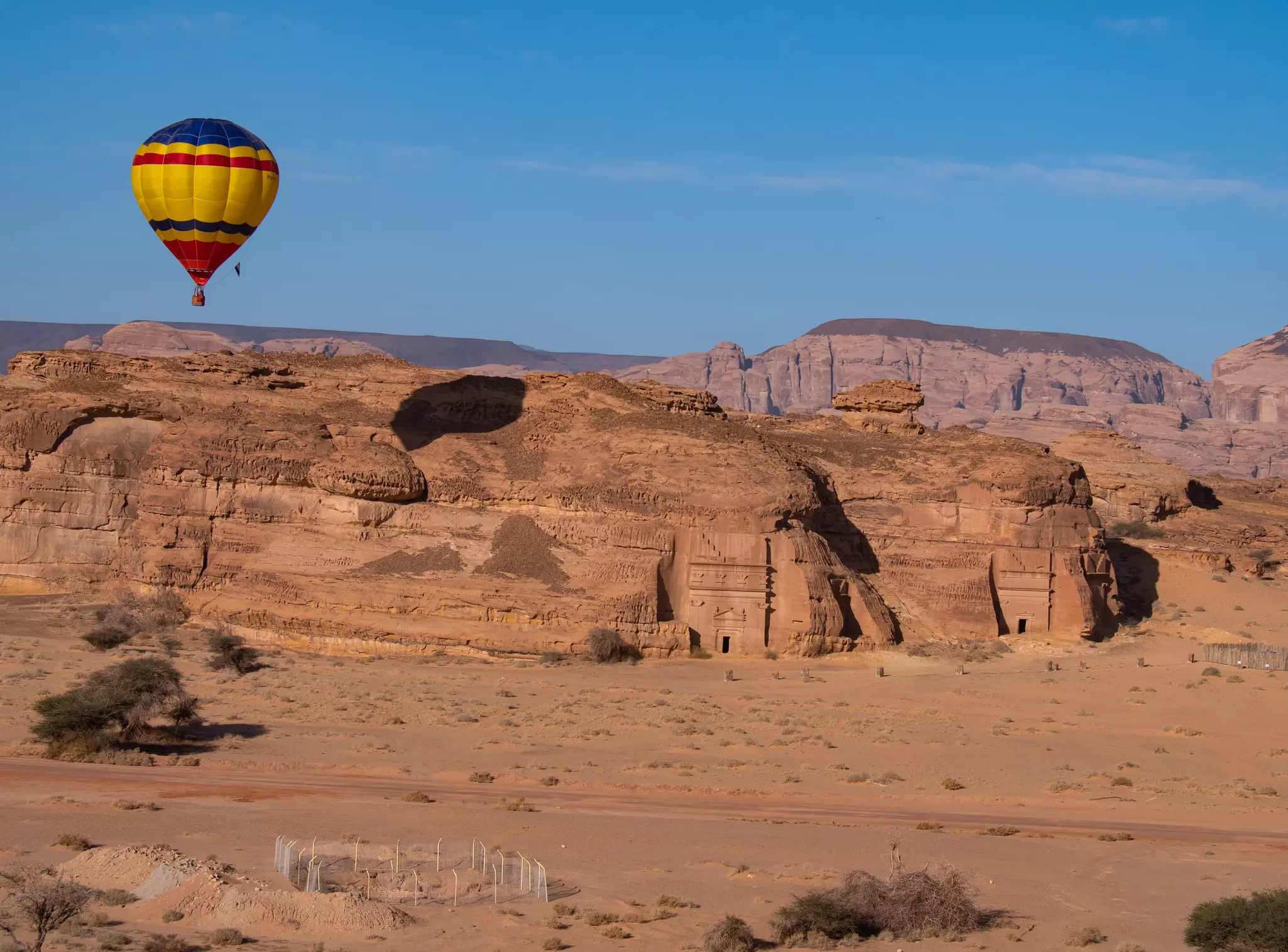 A multicolored hot-air balloon flies over over rock formations in a desert.