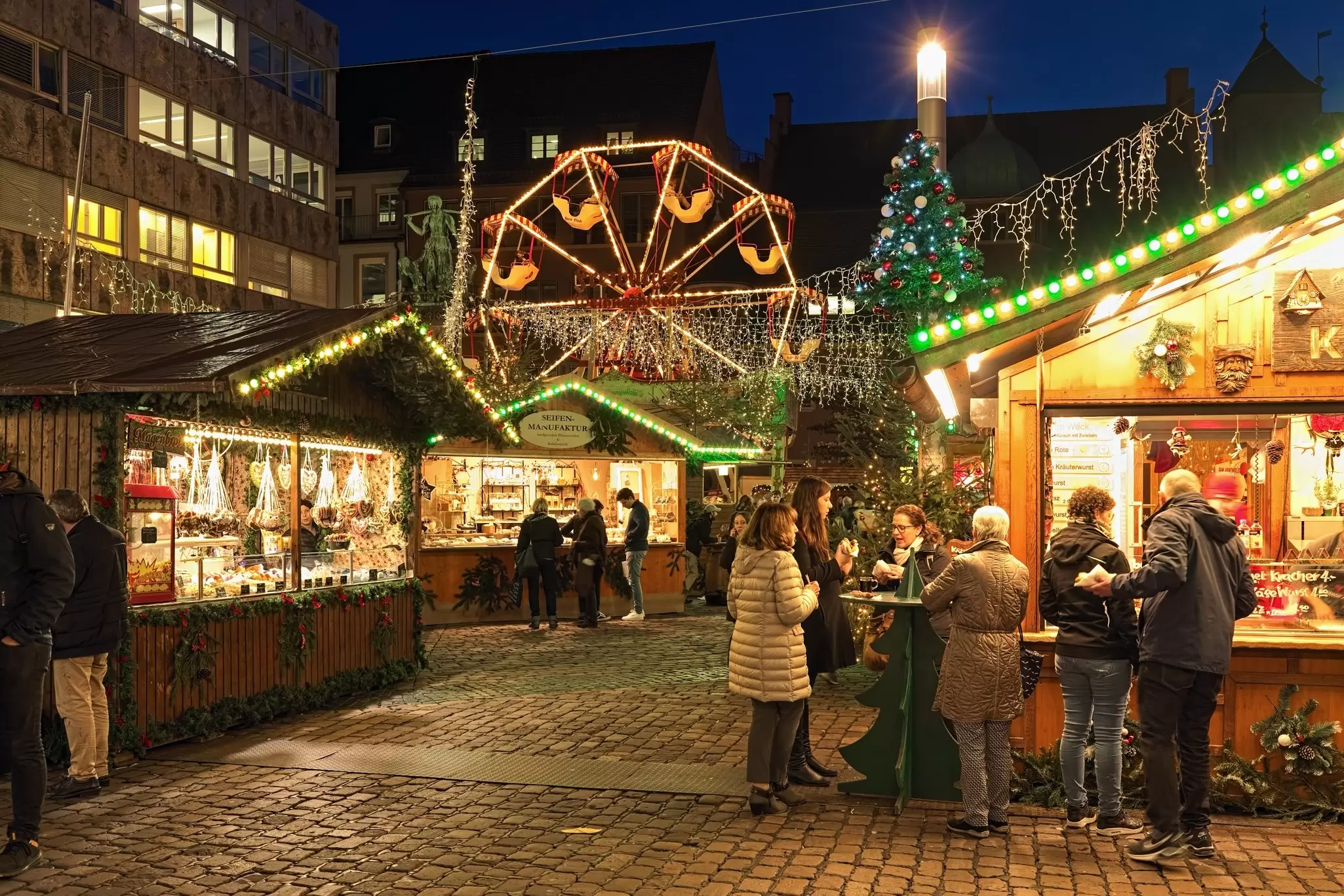 People eating by market stalls at night.