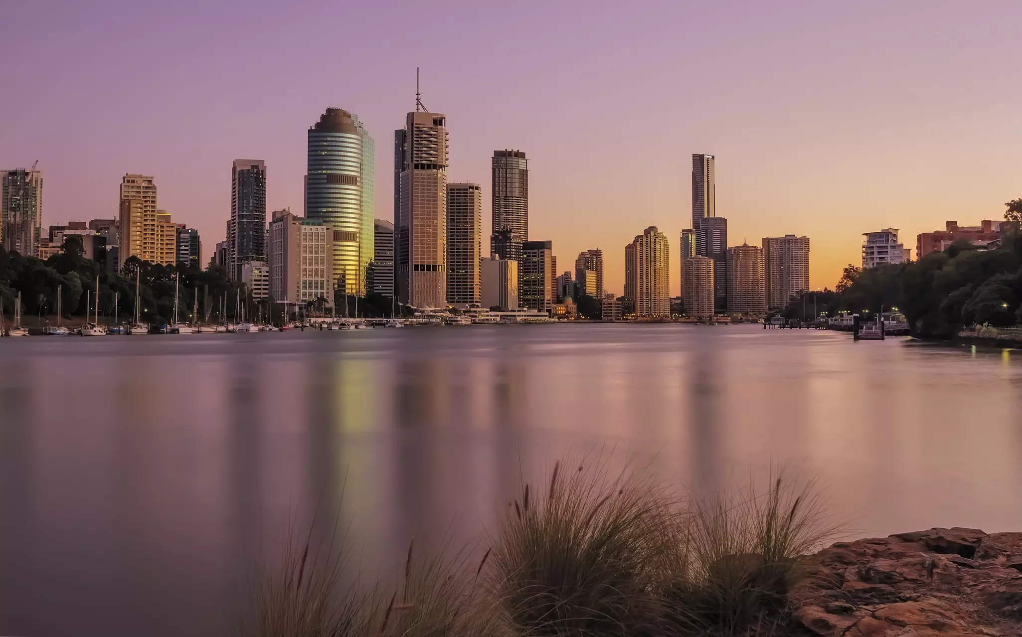 City skyline at sunrise with pinkish hue on water in the foreground.