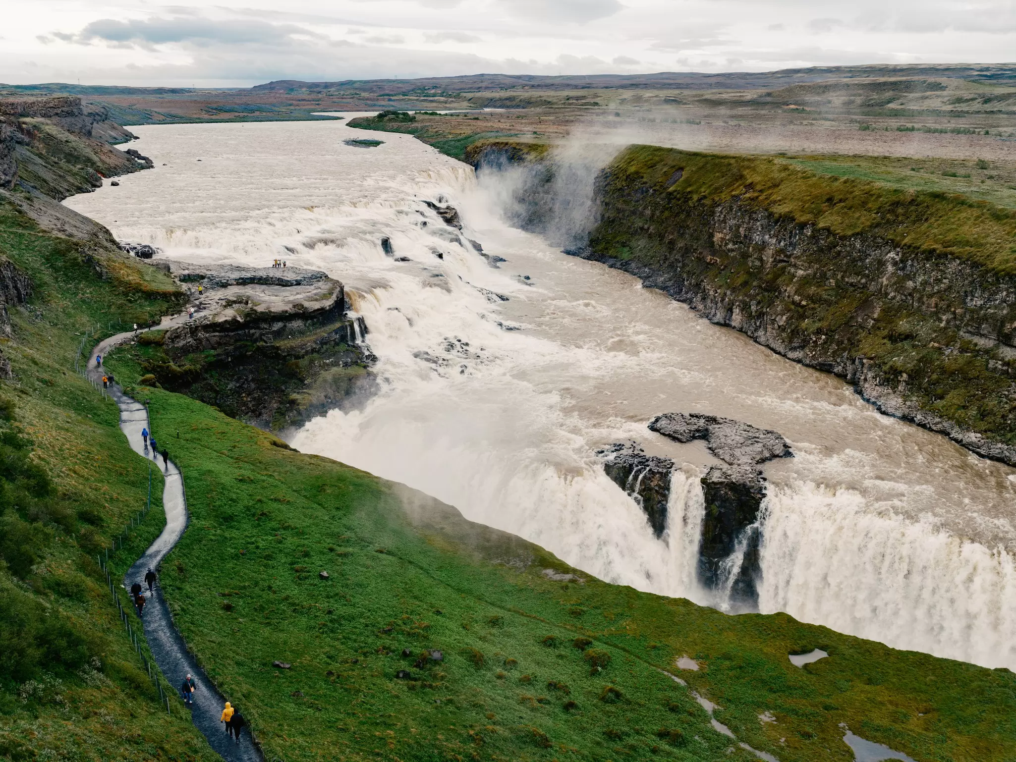 A massive waterfall; a narrow path through grass runs alongside.