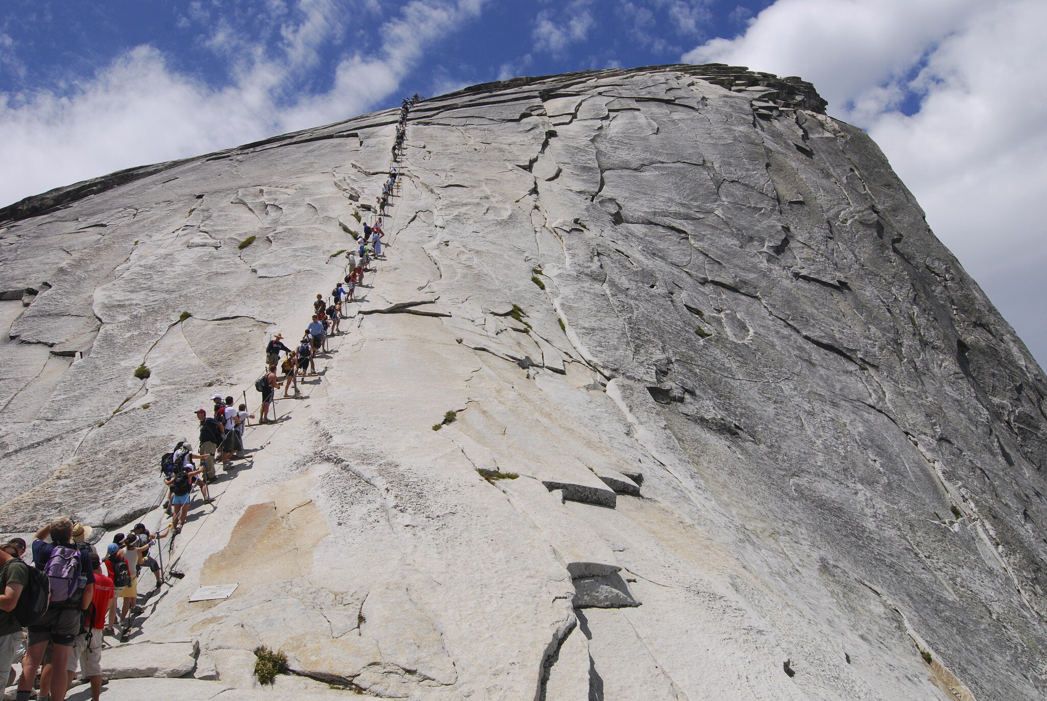People trekking single file betwen cables up a gray mountain peak