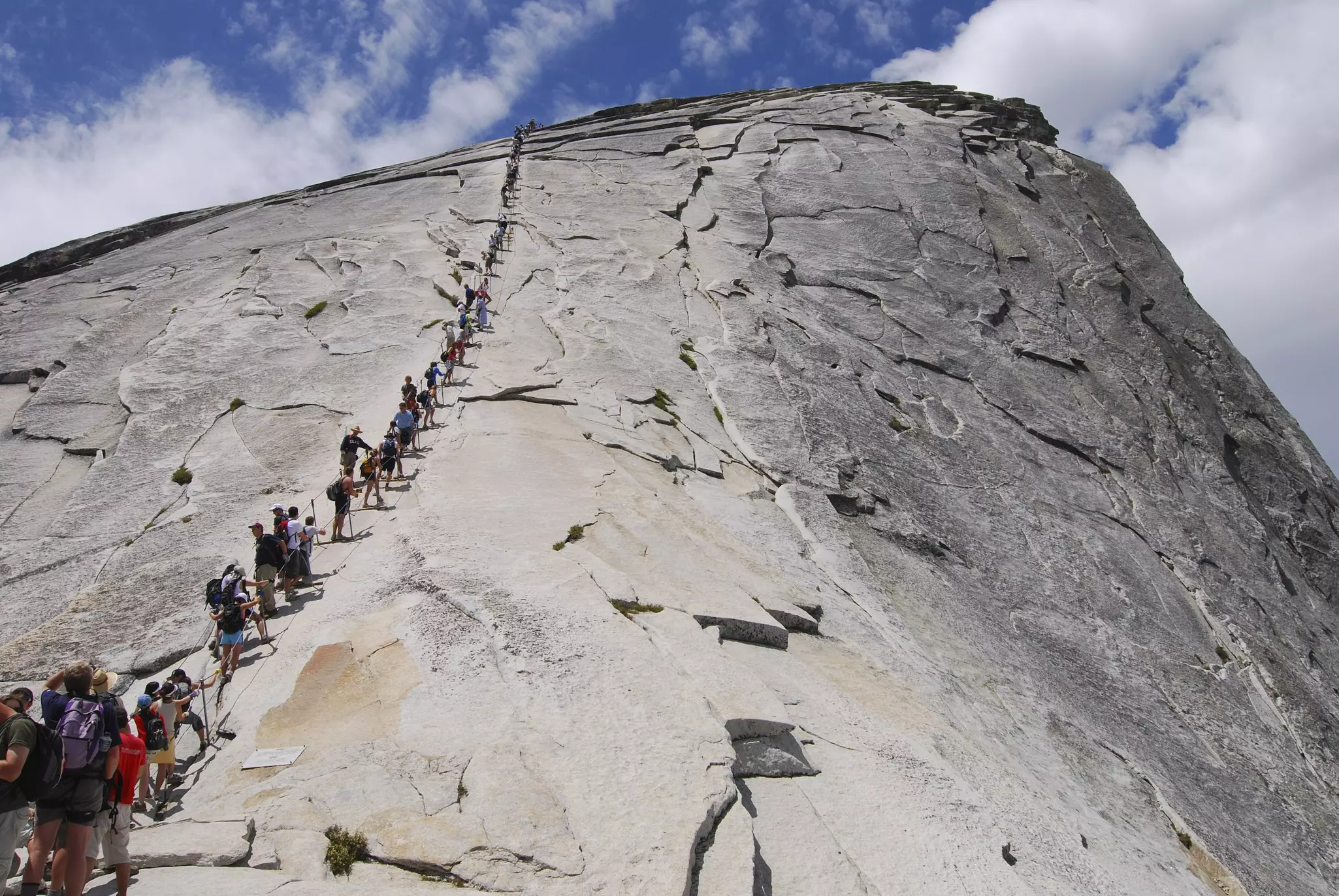 People trekking single file betwen cables up a gray mountain peak