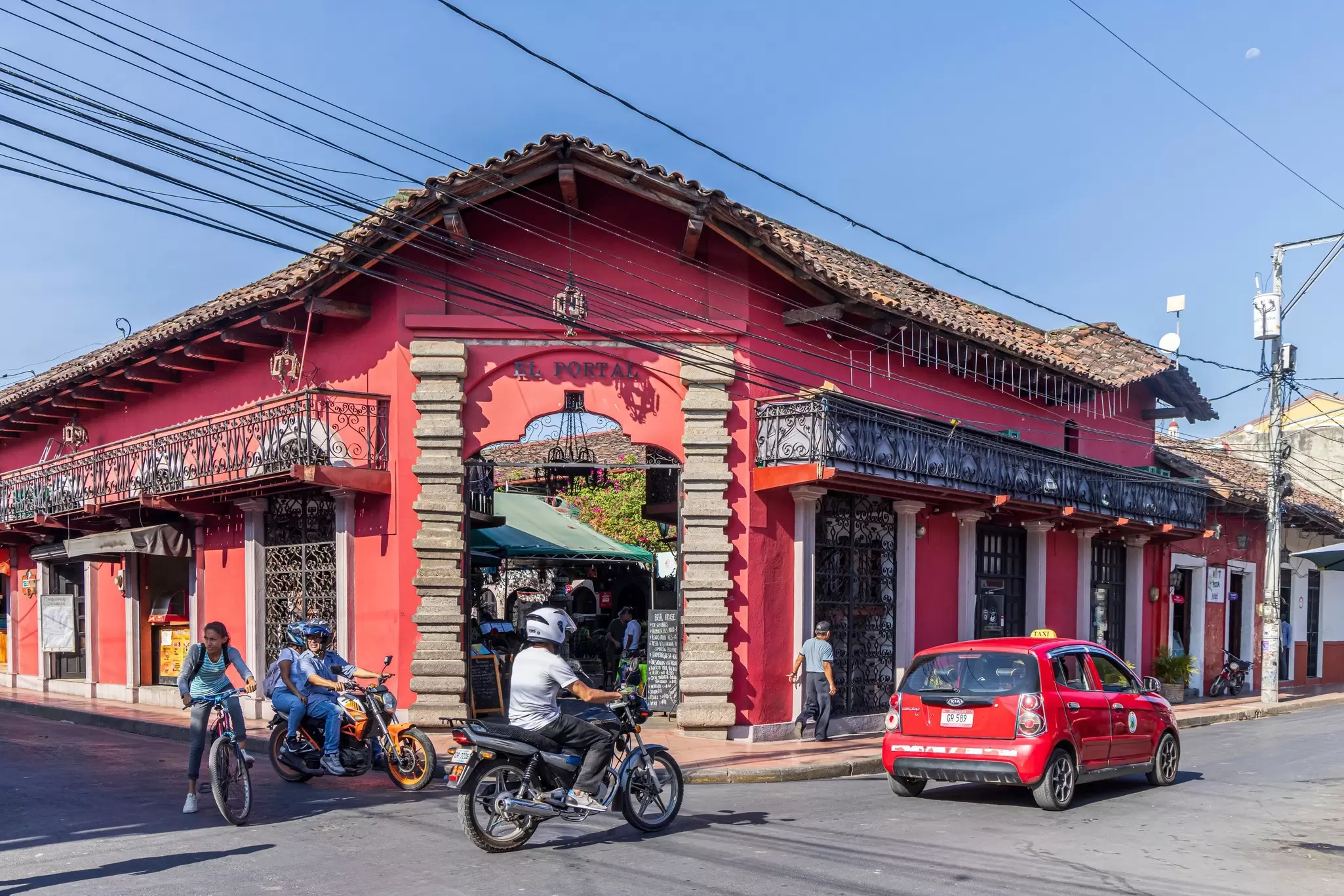 Motorcycles and cars drive past a pink-painted, single-story building in Granada, Nicaragua