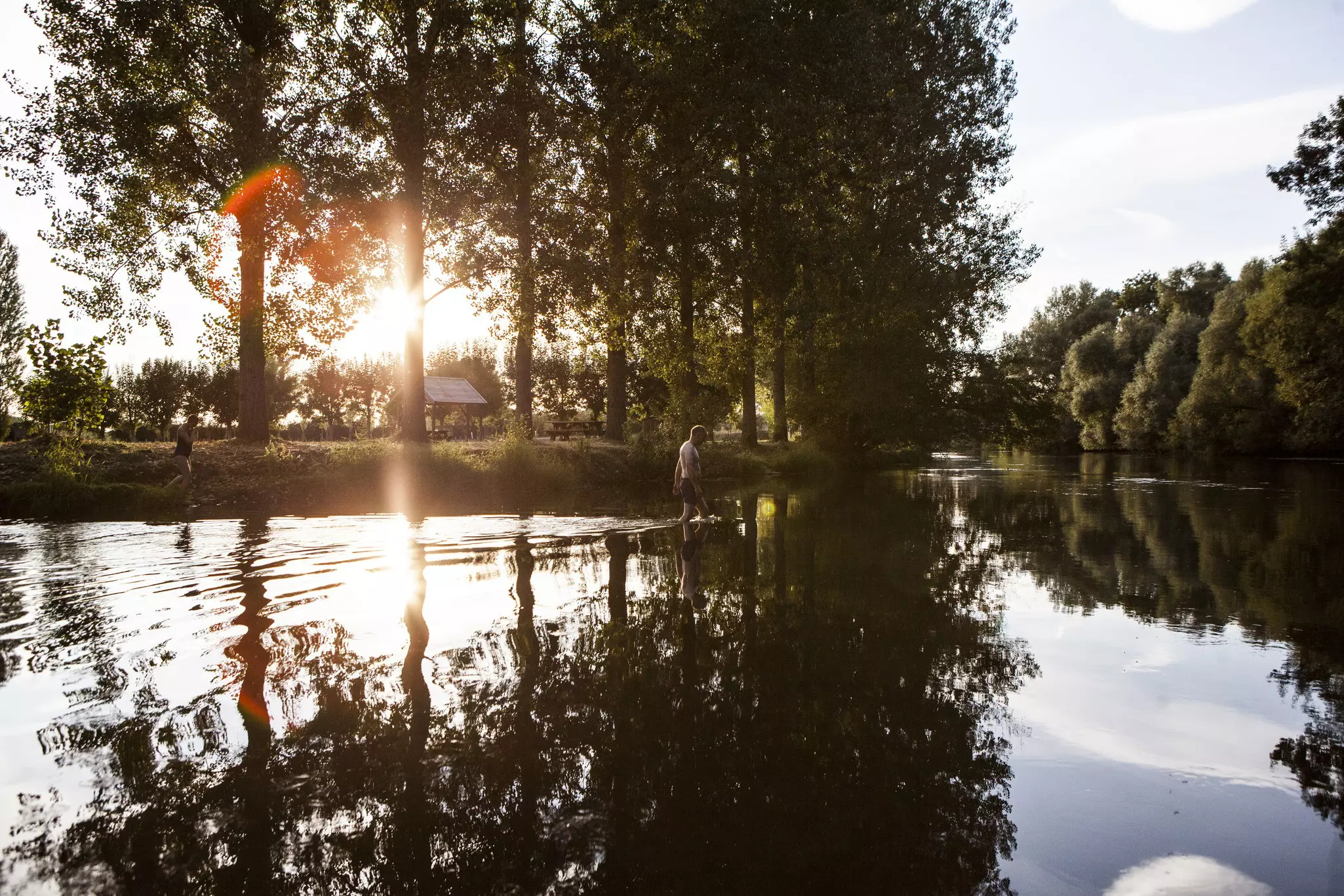 Sunlight through trees on a canal in France with a man striding through the water