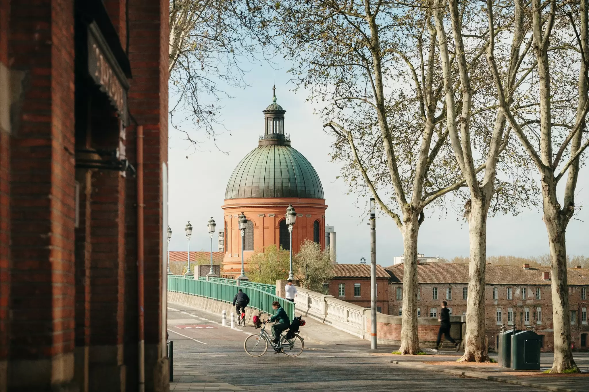 A red building with a dome is on the other side of a bridge where there is a pedestrian and a cyclist.
