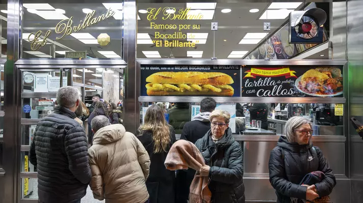 People line up to buy a squid sandwich at a glass-fronted place called "El Brillante"